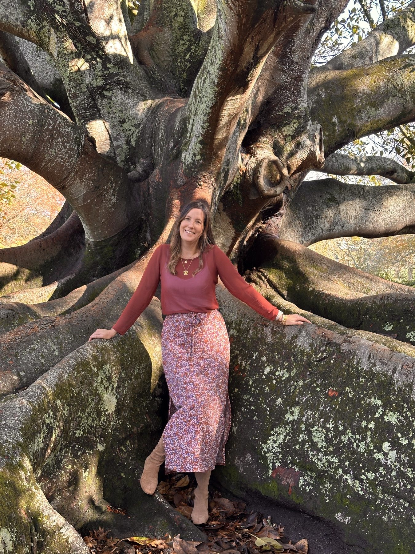 Gianna Degueldre standing among the expansive roots of a sunlit tree