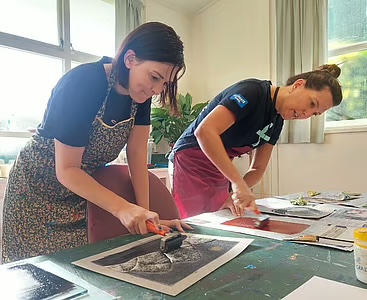 Two people exploring printmaking with rollers and art materials at a studio table
